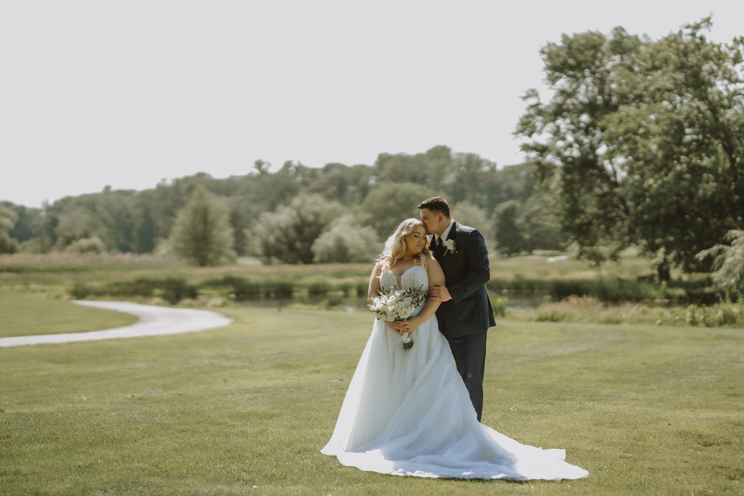 A groom kissing the top of his brides head with the golf course in the background at The Clubhouse at Galloping Hill in Kenilworth, New Jersey