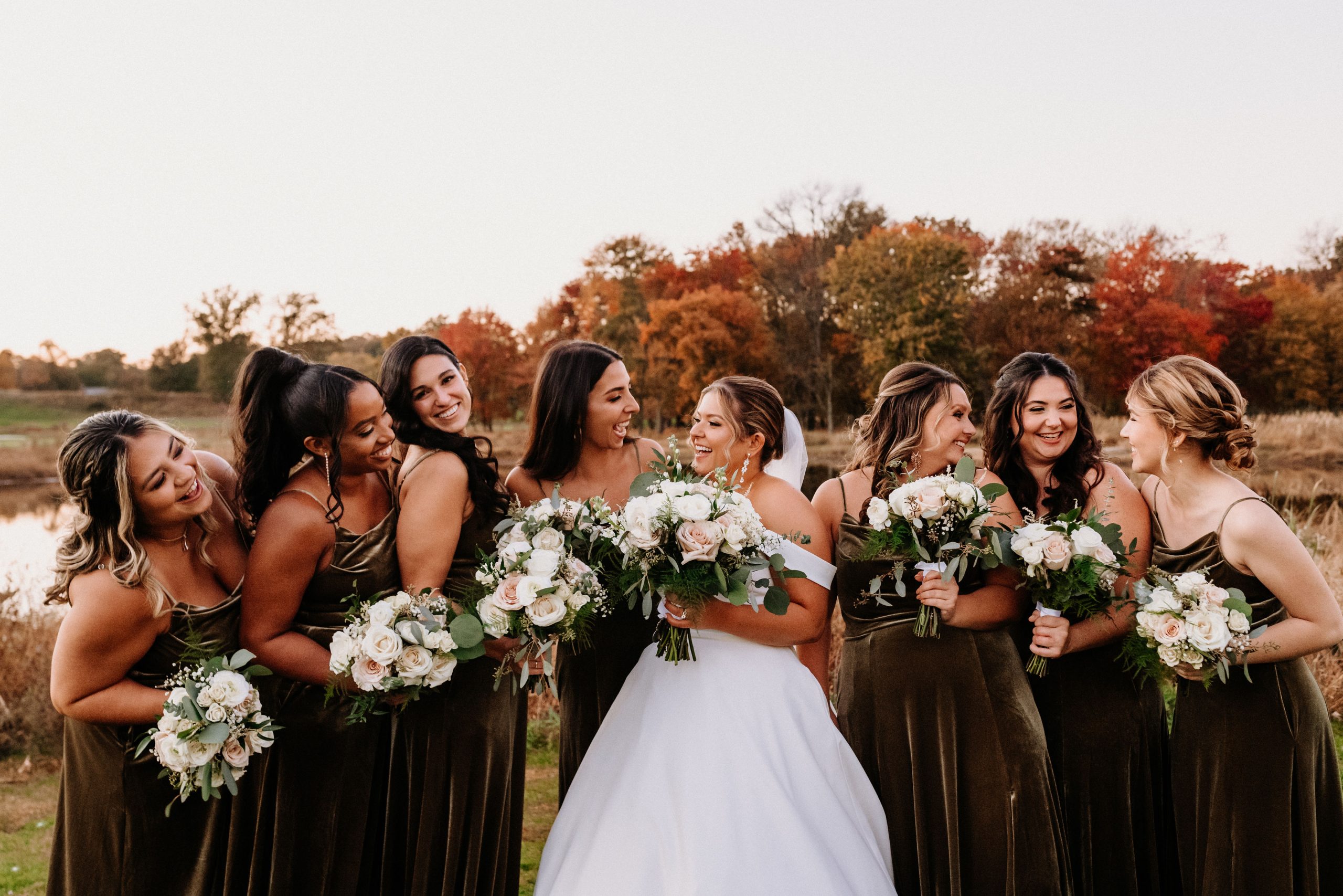 A bride and her bridesmaids outside in front of autumn foliage at The Clubhouse at Galloping Hill in Kenilworth, New Jersey