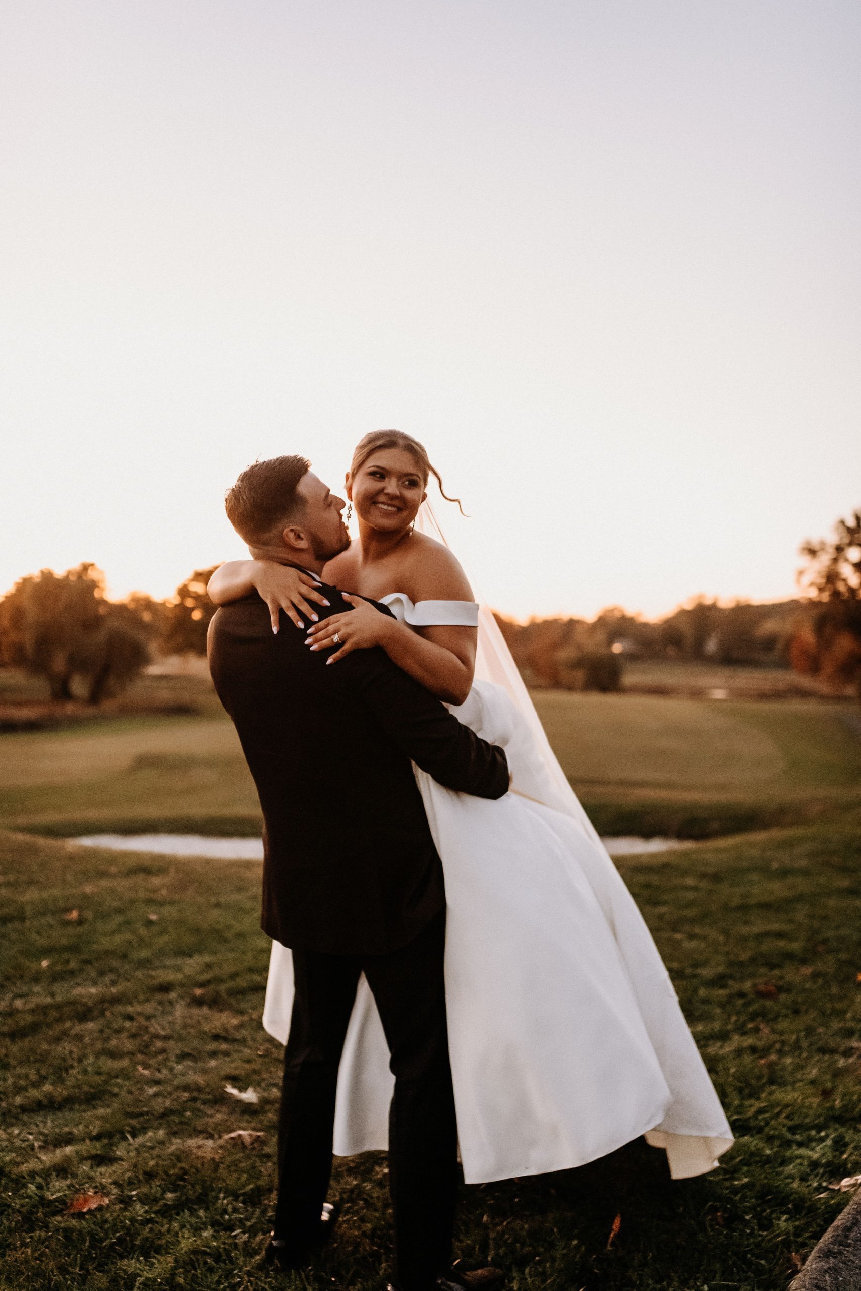 A bride being lifted up by her groom on the golf course at The Clubhouse at Galloping Hill in Kenilworth, New Jersey