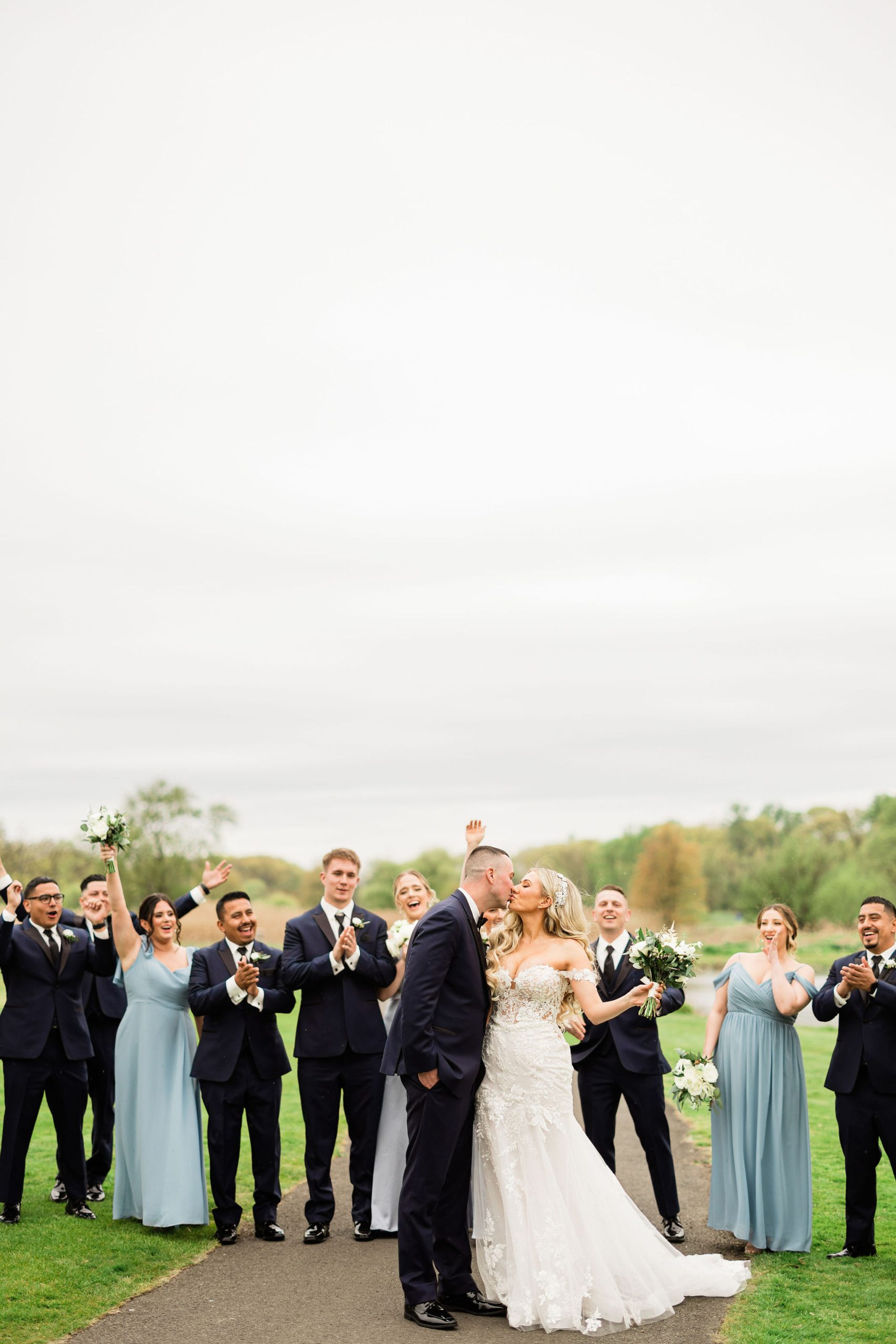 A bride and groom kissing in front of their cheering wedding party outdoors at The Clubhouse at Galloping Hill in Kenilworth, New Jersey