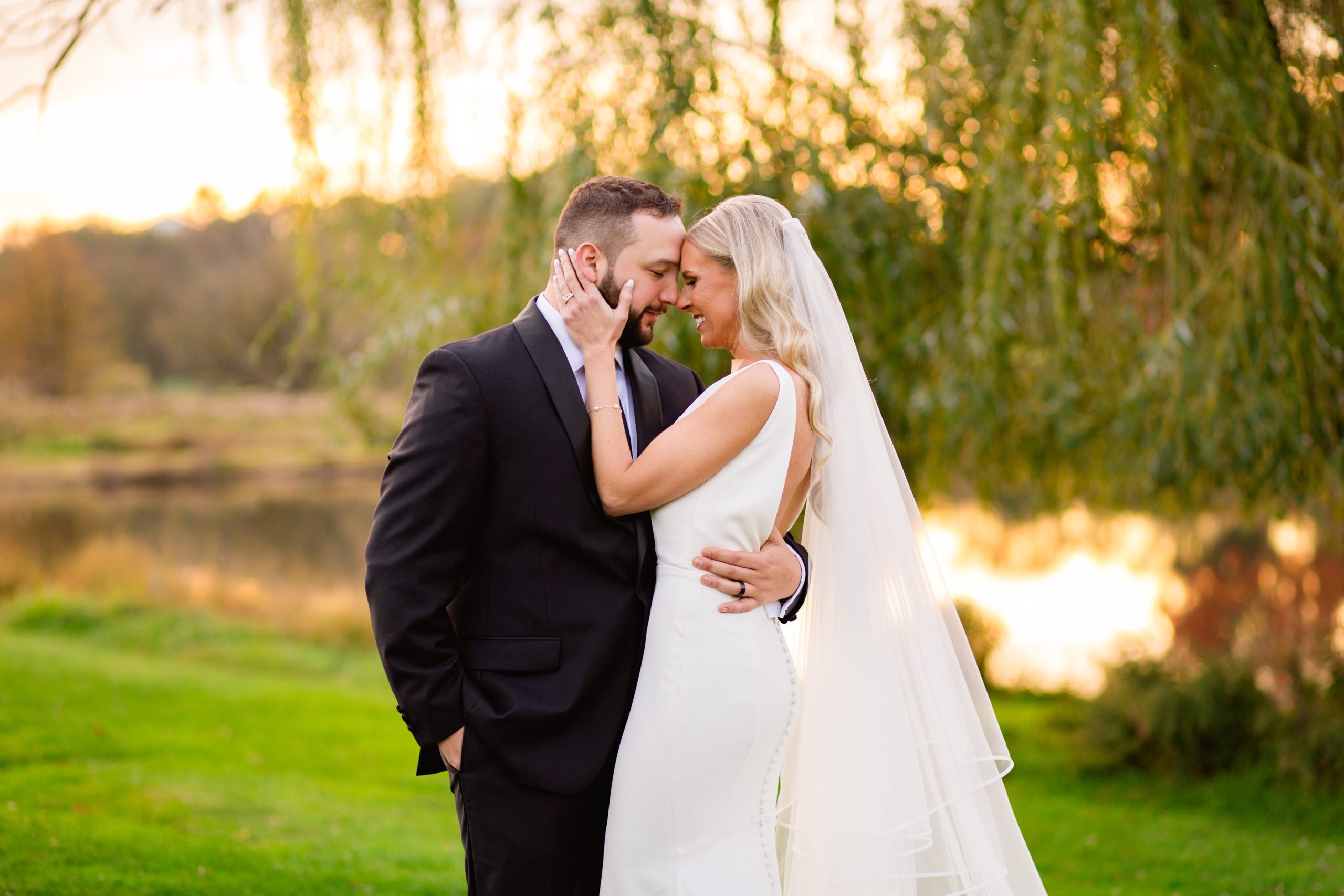A bride and groom embrace in front of a pond and willow tree on the golf course at The Clubhouse at Galloping Hill in Kenilworth, New Jersey