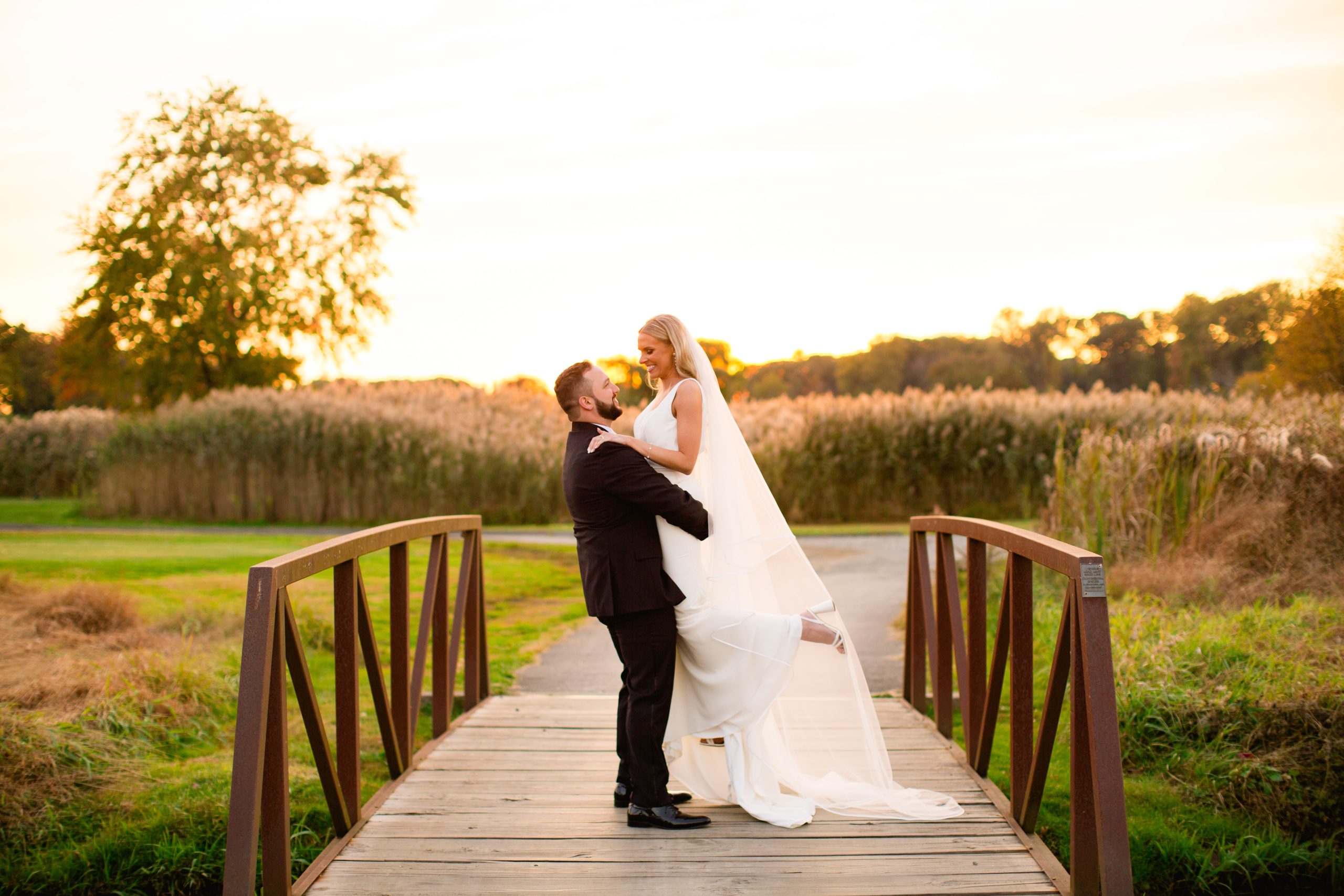 A groom holding up his bride at sunset on a bridge on the golf course at The Clubhouse at Galloping Hill in Kenilworth, New Jersey