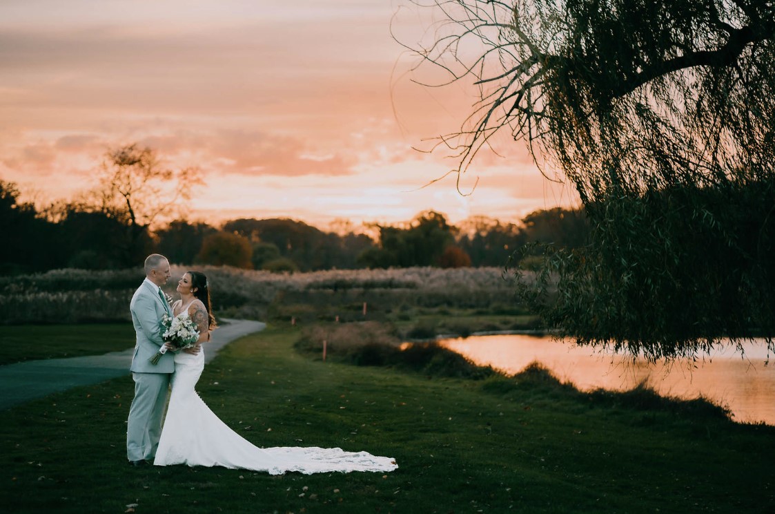 A bride and groom stand on the golf course in front of a pond at The Clubhouse at Galloping Hill in Kenilworth, New Jersey